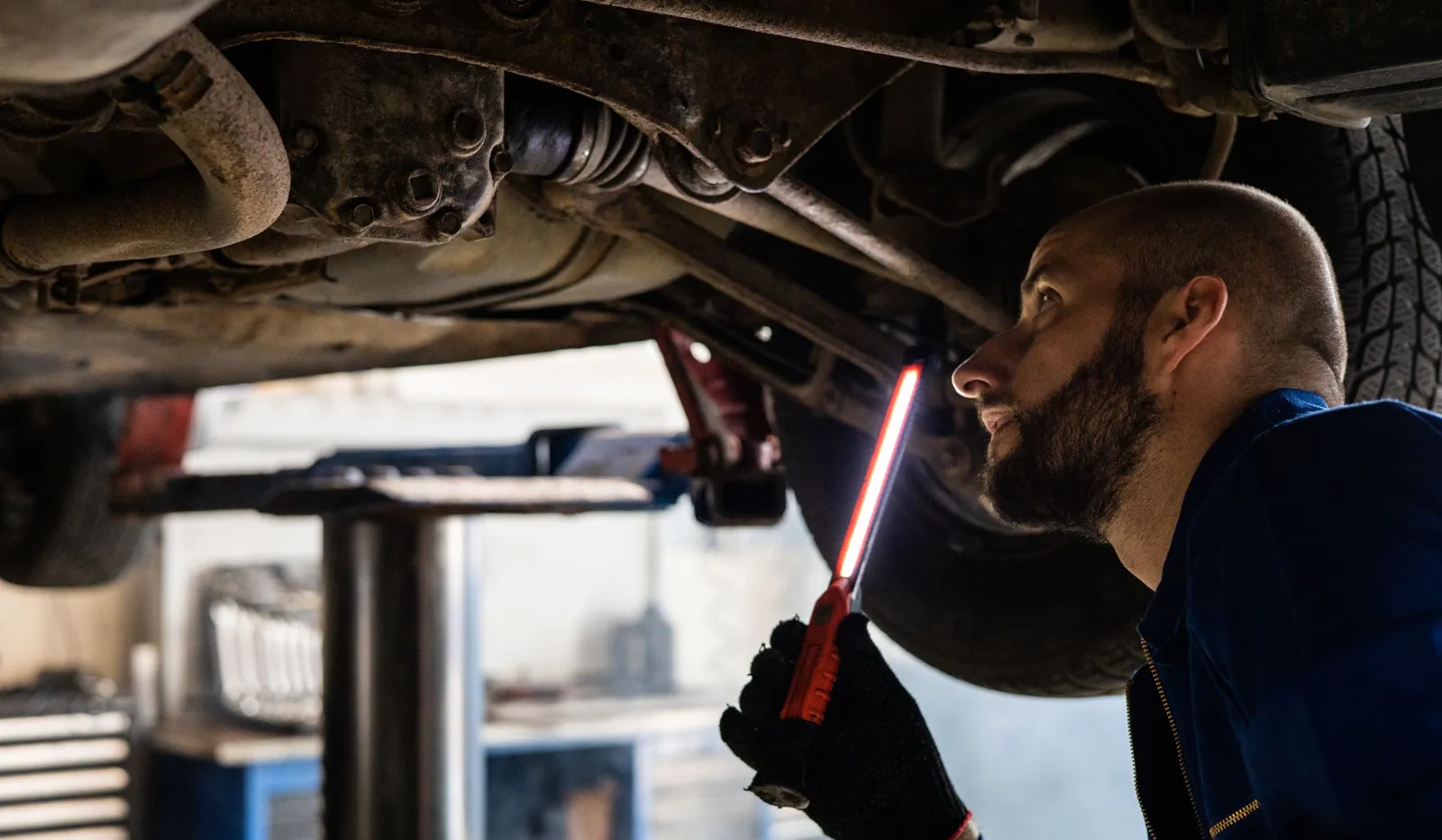 Mecánico revisando con una linterna los bajos de un coche elevado en el taller